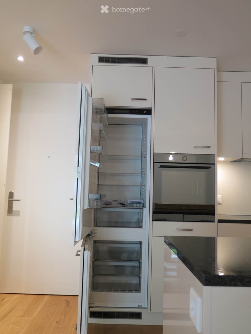 Modern kitchen with white cabinets, stainless steel appliances including a refrigerator and oven, and a black countertop.