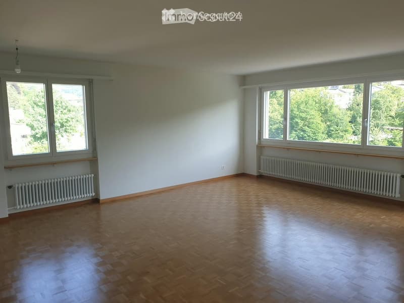 Empty room with wooden flooring, large windows, radiators, and white walls.