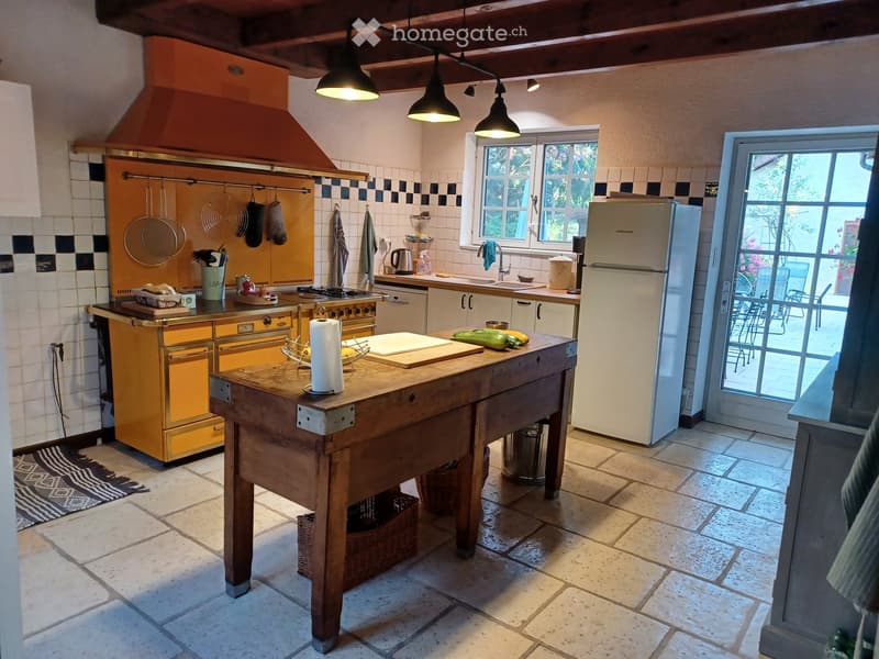 The kitchen features a wooden island, a vintage yellow stove, a refrigerator, and a sink with a window above it. The space includes hanging pots, a cutting board, and various kitchen utensils.
