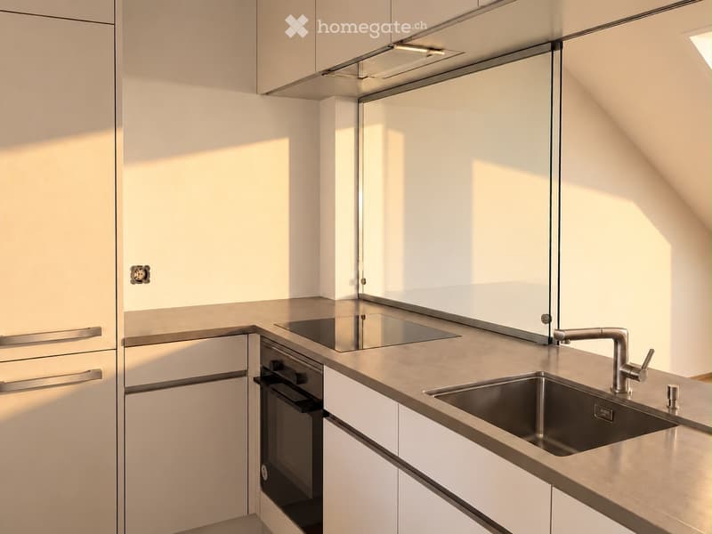 Modern kitchen with white cabinets, stainless steel sink, faucet, and built-in oven. Features a sleek, minimalist design with ample natural light.