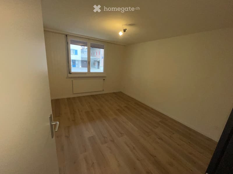 Empty room with light wooden flooring, white walls, and a window with a radiator below it.