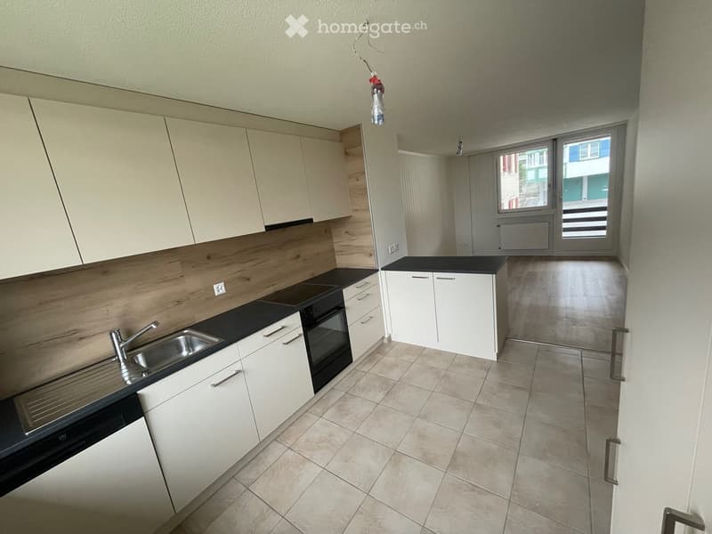 Modern kitchen with white cabinets, black countertops, a sink, and an oven. The space features tiled flooring and a window with a view of the outside.