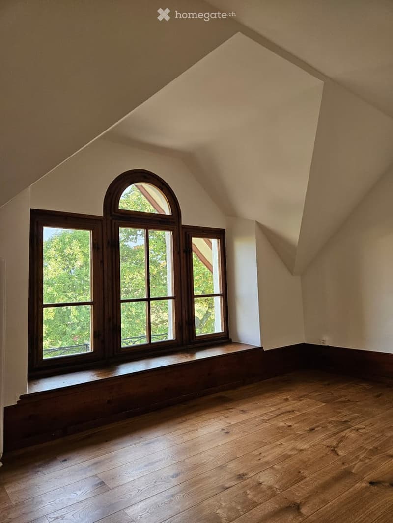 Empty attic room with wooden floors, large windows, and slanted ceilings.