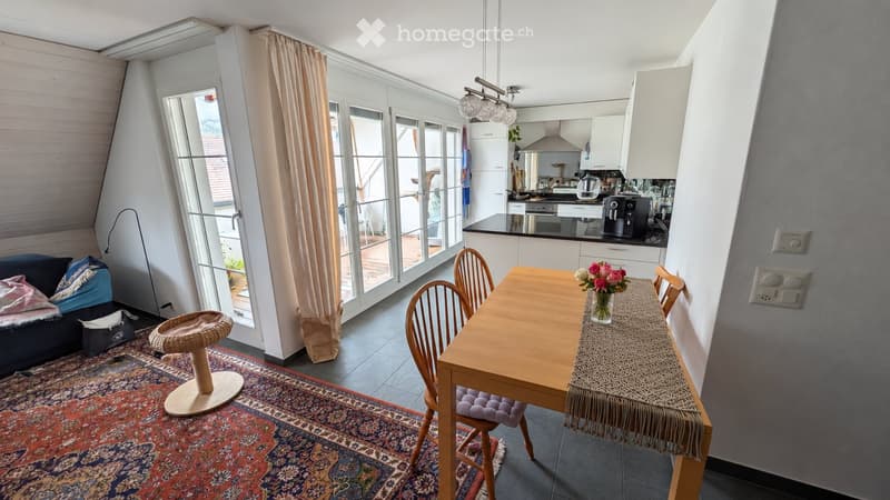 Bright living and dining area with large windows, a sofa, a dining table with chairs, a cat tree, and a kitchen area with appliances.