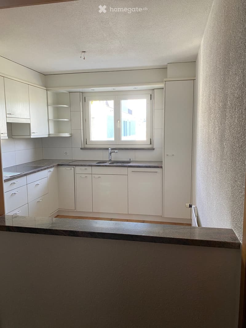 Modern kitchen with white cabinets, a sink, and a countertop, featuring a window above the sink and a bar area in the foreground.