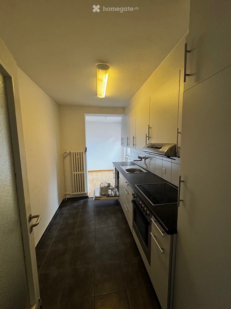 Modern kitchen with dark tiled floor, white cabinets, black countertop, sink, stove, oven, and dishwasher. Radiator visible on left wall.