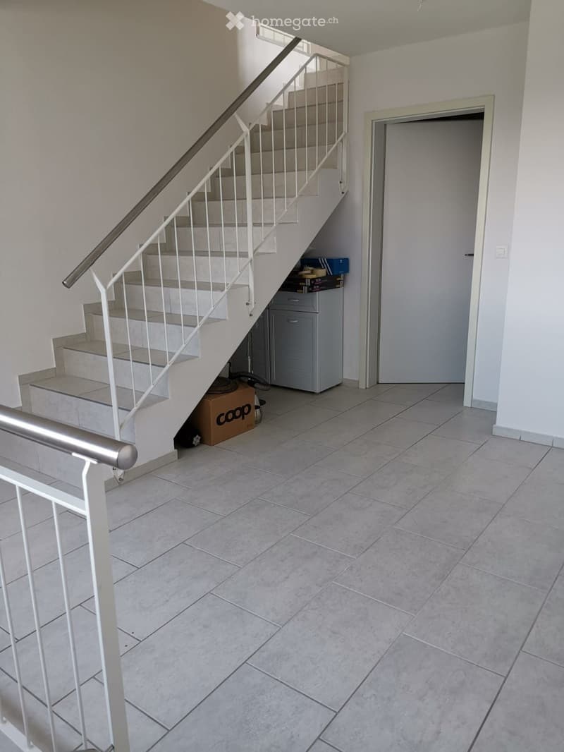 Empty hallway with tiled floor, staircase leading upwards, and a closed door on the right side.