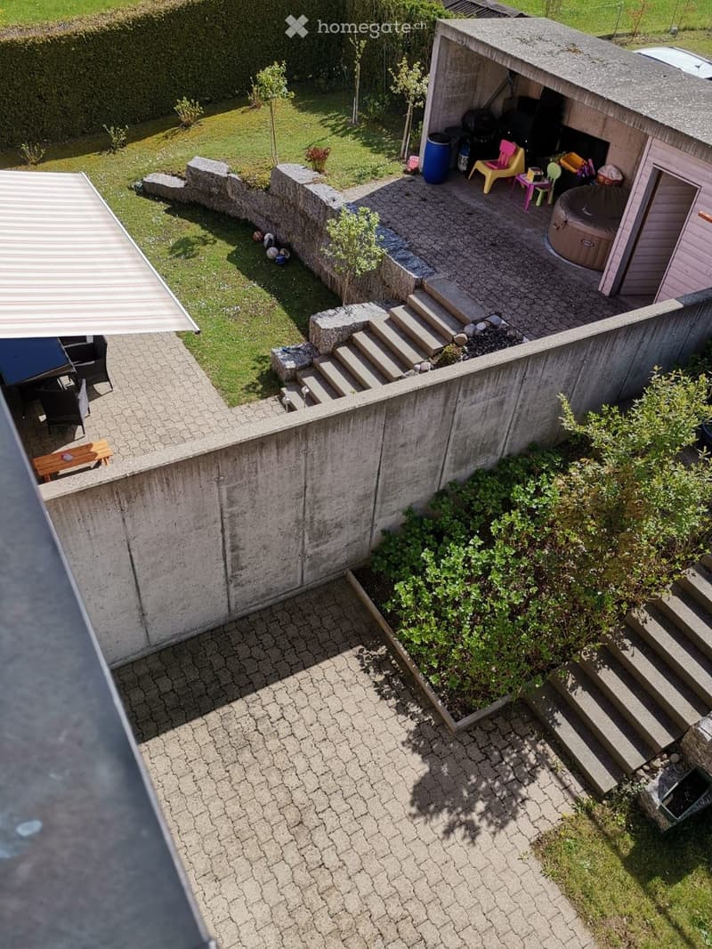Garden with a paved patio, small shed, hot tub, steps leading to a raised lawn area, and various plants and shrubs.