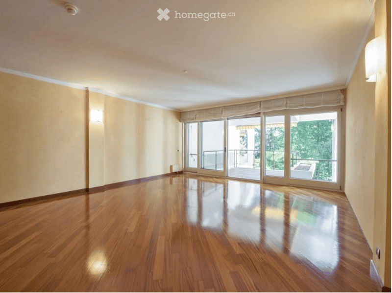 Empty room with polished wooden flooring, large windows, and a balcony accessible through sliding doors.