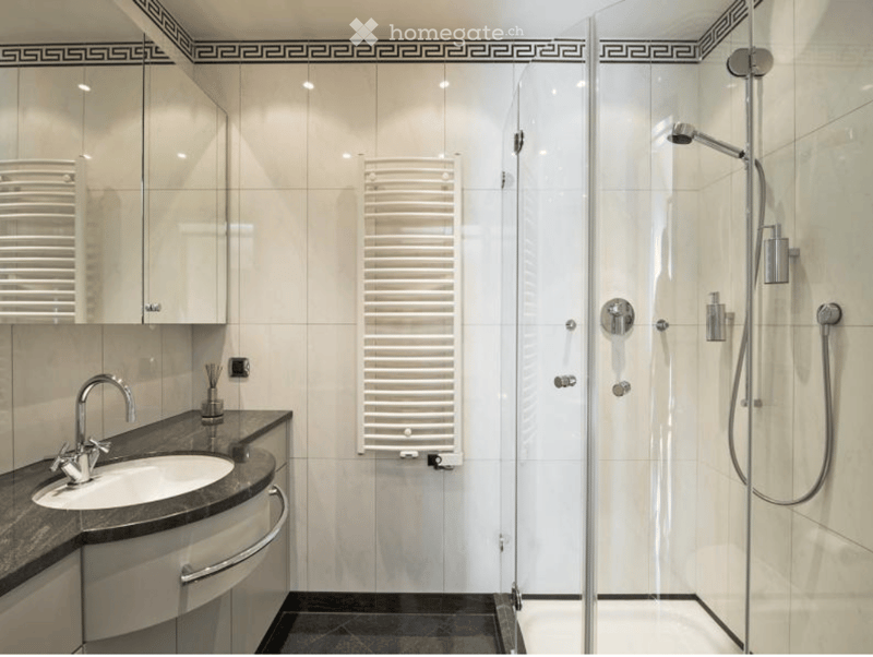 Modern bathroom with a white tiled shower enclosure, a sink with a chrome faucet, a built-in radiator, and a mirrored cabinet above the sink.