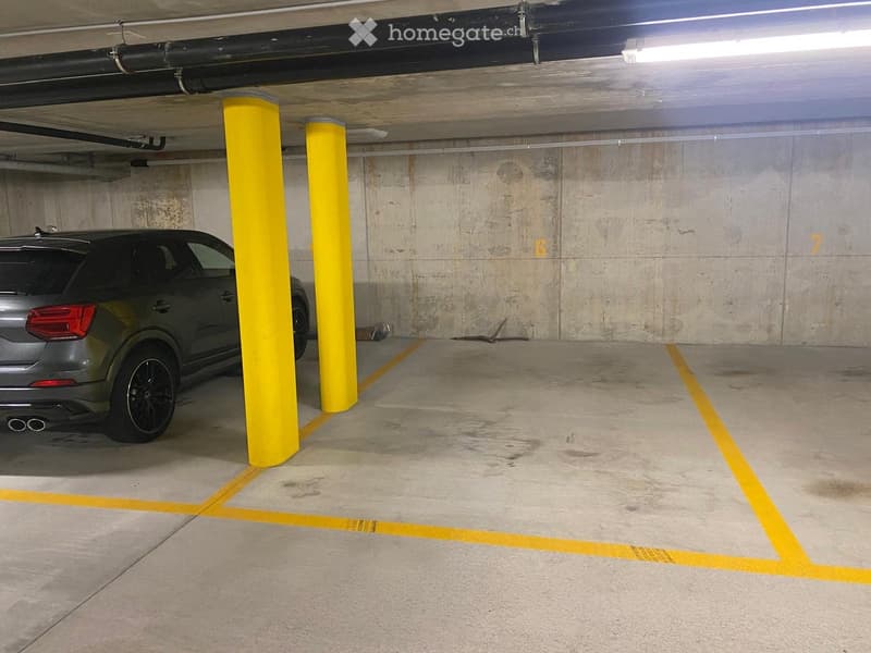 Underground parking area with concrete floors and walls, yellow parking dividers, and a parked car.
