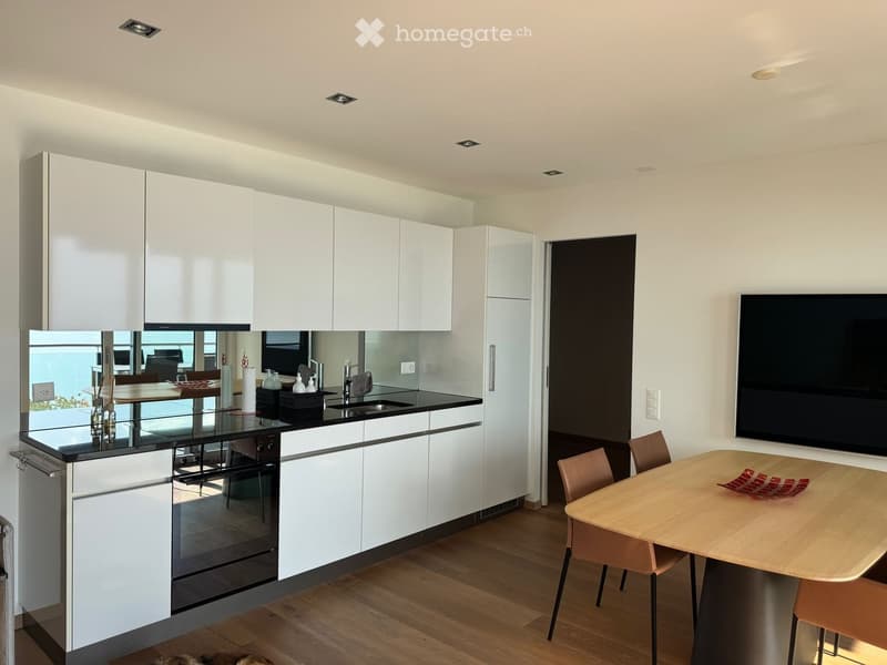 Modern kitchen with white cabinets, black countertops, stainless steel appliances, and a dining area with a wooden table and chairs.