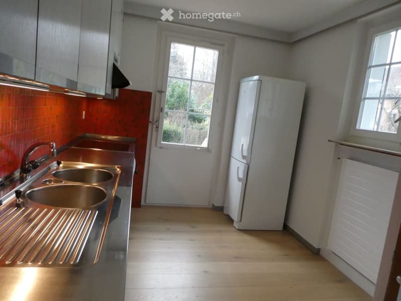 Modern kitchen with stainless steel sink, white refrigerator, and light wooden flooring.