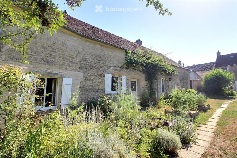 A rustic stone house with a well-maintained garden, featuring a variety of plants, a stone pathway, and a small lantern near the entrance.