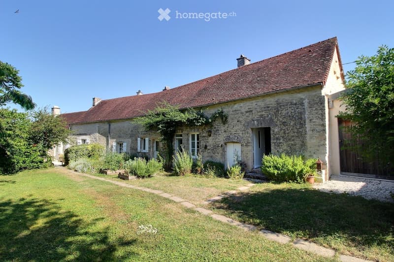 A rustic stone house with a red-tiled roof, surrounded by a well-maintained garden and pathway.