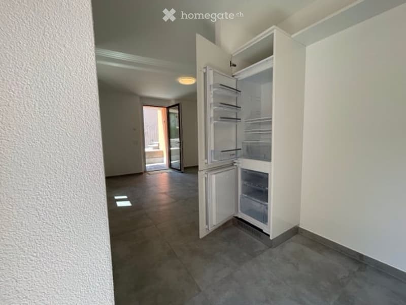 Empty kitchen area with a built-in refrigerator, tiled floor, and an open doorway leading to a balcony or outdoor area.