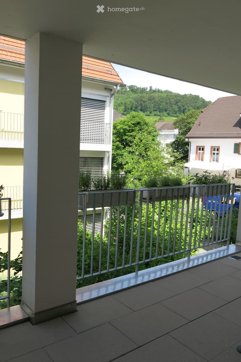 Balcony with tiled floor, metal railing, and view of greenery and neighboring buildings.