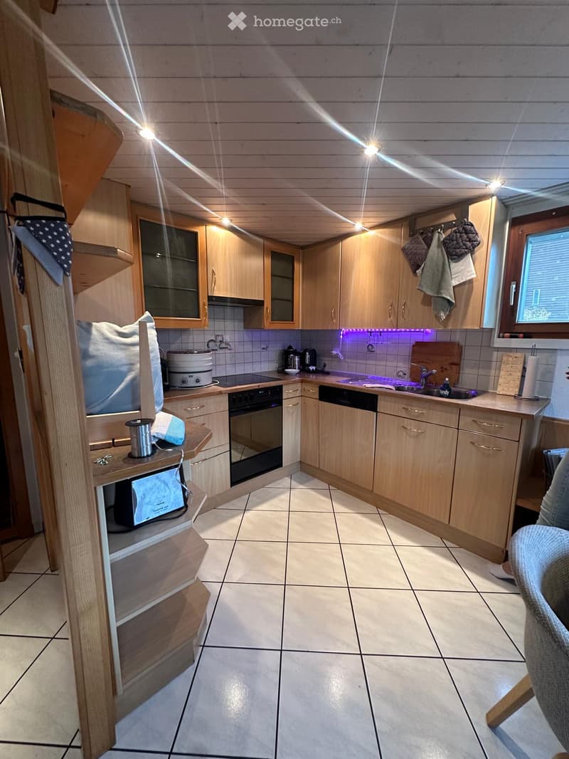Modern kitchen with light wooden cabinets, tiled floor, and various appliances including a microwave, oven, dishwasher, and sink.