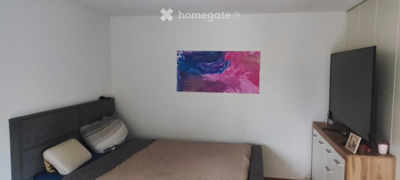 A modern bedroom with a bed, headboard, pillows, a nightstand, a painting on the wall, and a cup on the nightstand.