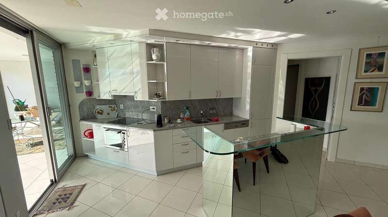 Modern kitchen with white cabinets, granite countertops, built-in oven, dishwasher, and a glass bar table with chairs.