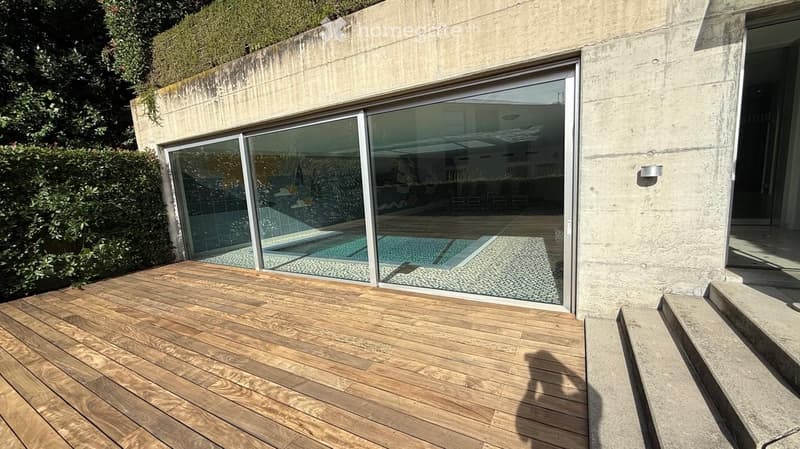 Wooden deck area with large glass sliding doors leading to an indoor space, with a swimming pool visible through the glass.