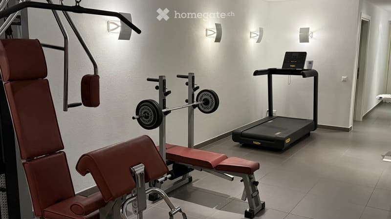 Well-lit gym room with a treadmill, weight bench, weight machine, and a laptop on the treadmill.