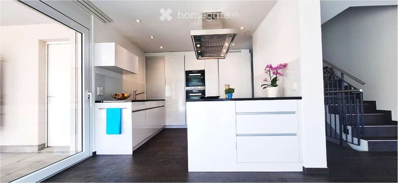 Modern kitchen with white cabinets, stainless steel appliances, dark wooden floor, and a small island with a countertop.