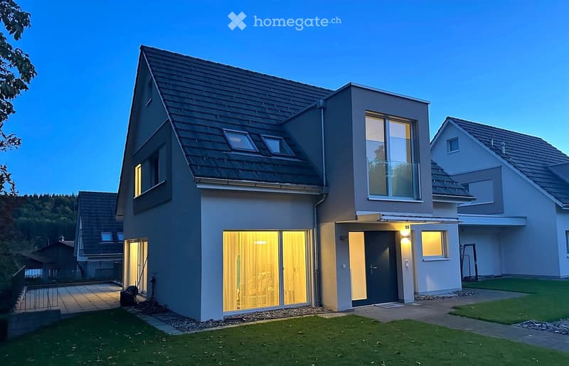 Modern two-story house with a sloped roof, large windows, and a well-maintained lawn in front.