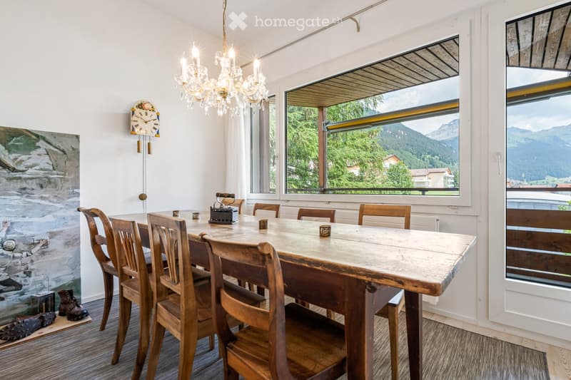 Dining room with a wooden table and chairs, chandelier, large windows offering a mountain view, and a painting on the wall.