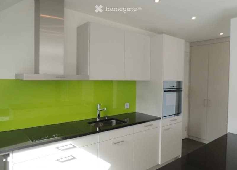 Modern kitchen with white cabinets, green backsplash, black countertop, and stainless steel appliances including a sink, faucet, and oven.