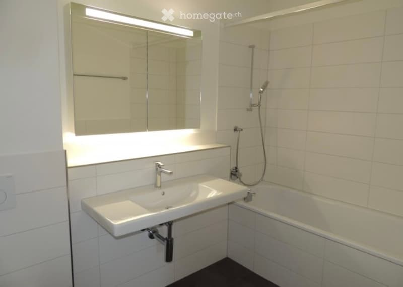 Modern bathroom with white tiles, a sink, a bathtub, and a large mirror with built-in lighting.