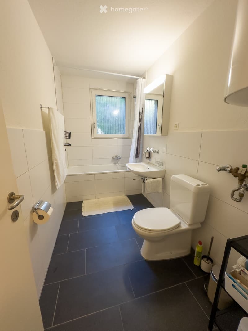 Modern bathroom with white tiles, blue floor, toilet, sink, bathtub, mirror, and towel.