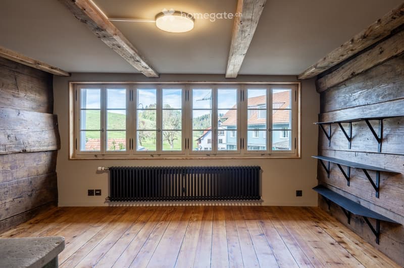 Empty room with wooden floors, exposed wooden beams, large windows, and built-in shelves.