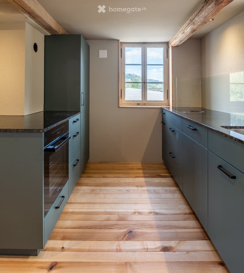 Modern kitchen with grey cabinets, wooden flooring, and a large window offering a scenic view.