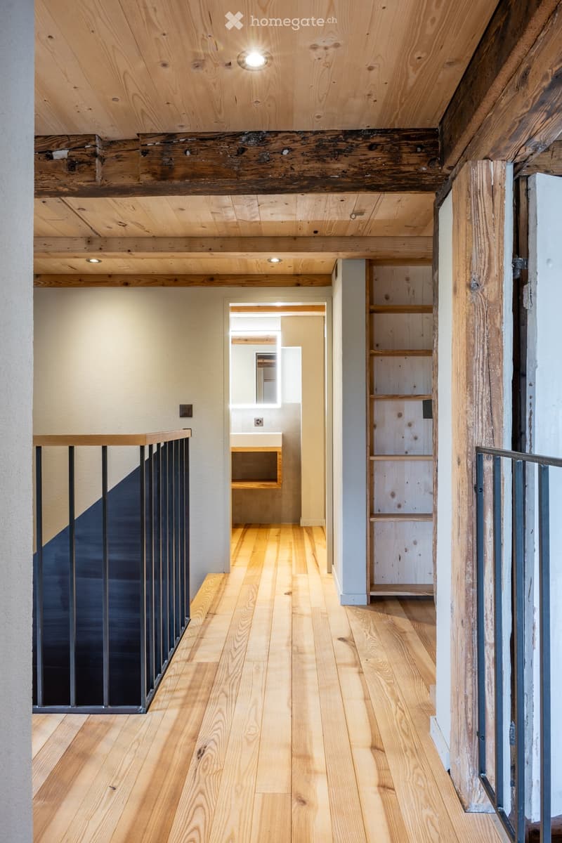 Wooden-floored hallway with exposed wooden beams, modern lighting, and a small built-in shelf unit on the right side.