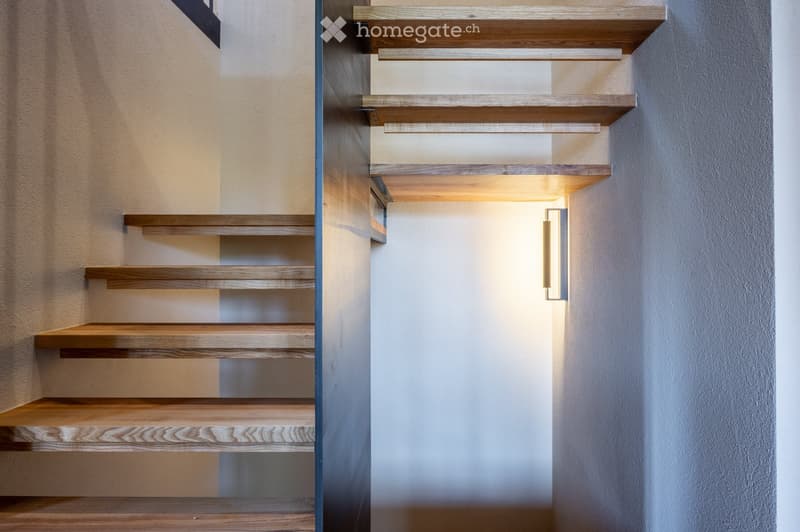 Modern staircase with wooden steps and sleek railings, illuminated by integrated lighting on the wall.