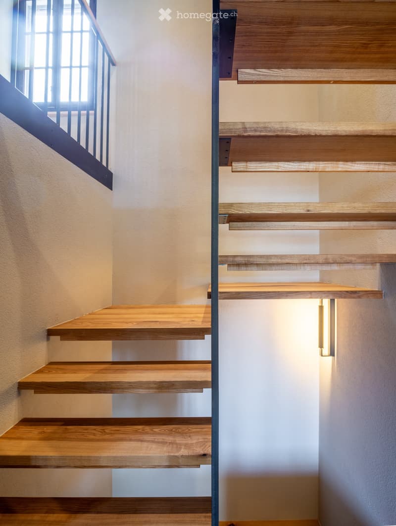 Modern wooden staircase with sleek design, integrated lighting, and a metal railing, leading upwards.