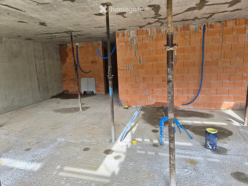 Empty basement or garage space with exposed brick walls, concrete floor, and various pipes and construction materials scattered around.