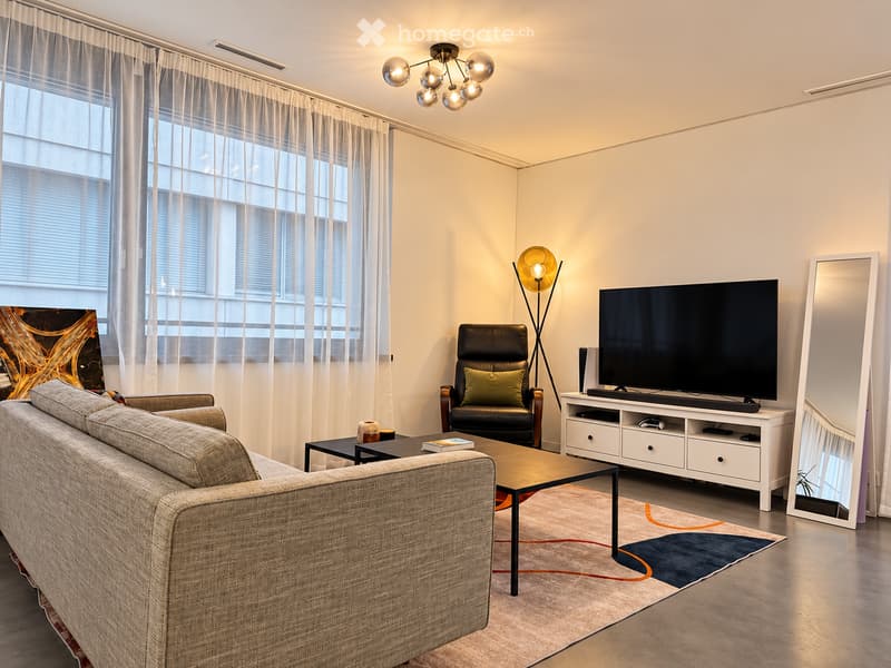 Modern living room with large windows, grey sofa, coffee table, armchair, TV, TV stand, floor lamp, and mirror.