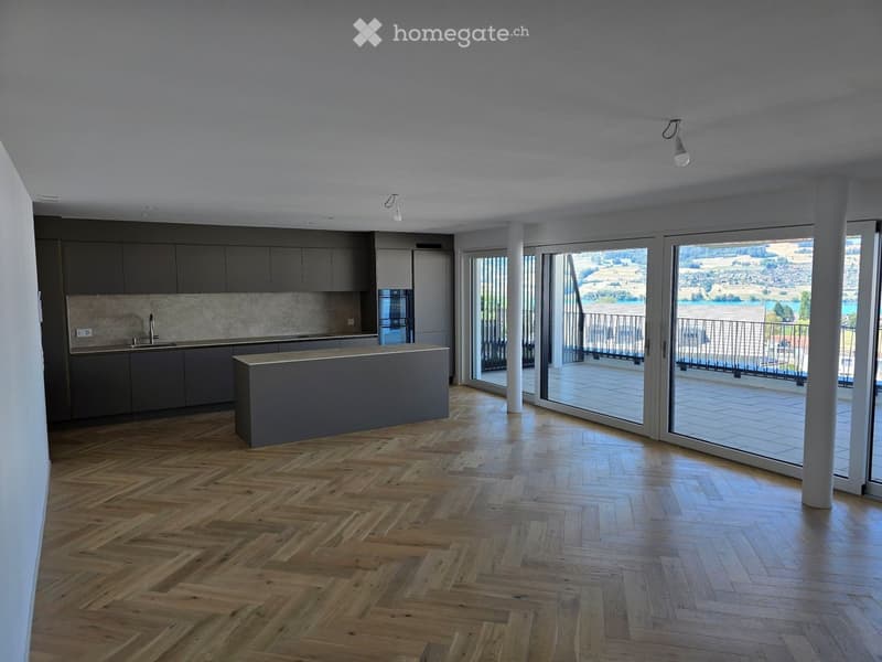 Modern kitchen with grey cabinets, a central island, and large windows offering a scenic view of the landscape.
