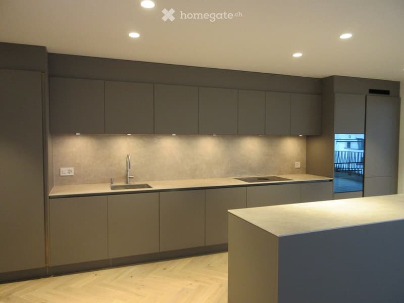 Modern kitchen with grey cabinets, a central island, and a sink with a faucet. The space features recessed lighting and a sleek design.