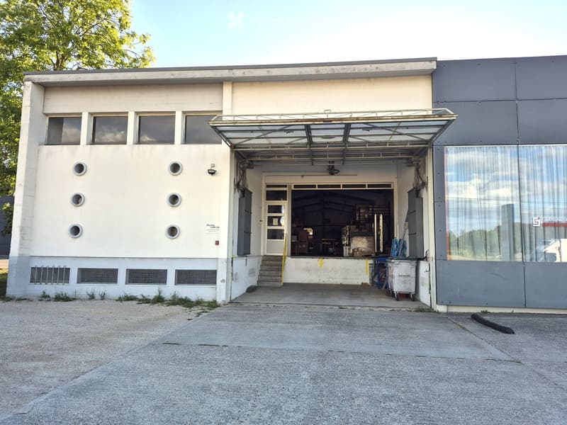 Two-story industrial building with a large garage entrance, circular windows, and a covered walkway.