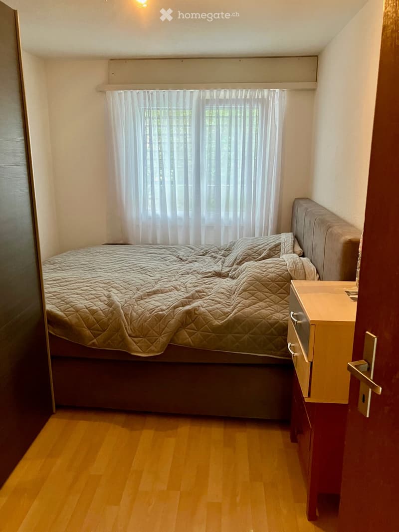 Cozy bedroom with a single bed, quilted duvet, nightstand, and window with white curtains.