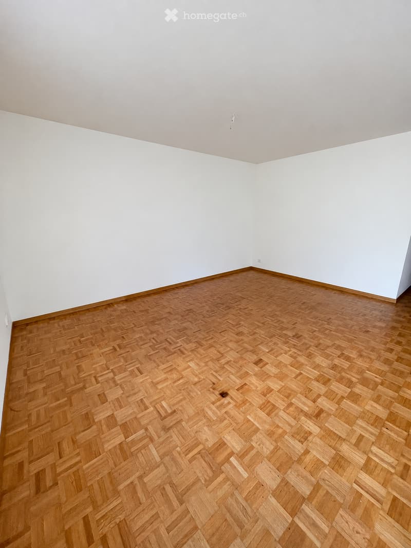 Completely empty room with bare white walls and a herringbone-patterned wooden floor. No furniture or equipment.