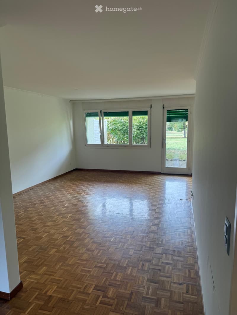 Empty room with wooden parquet flooring, white walls, large windows, and a sliding glass door leading to an outdoor area.