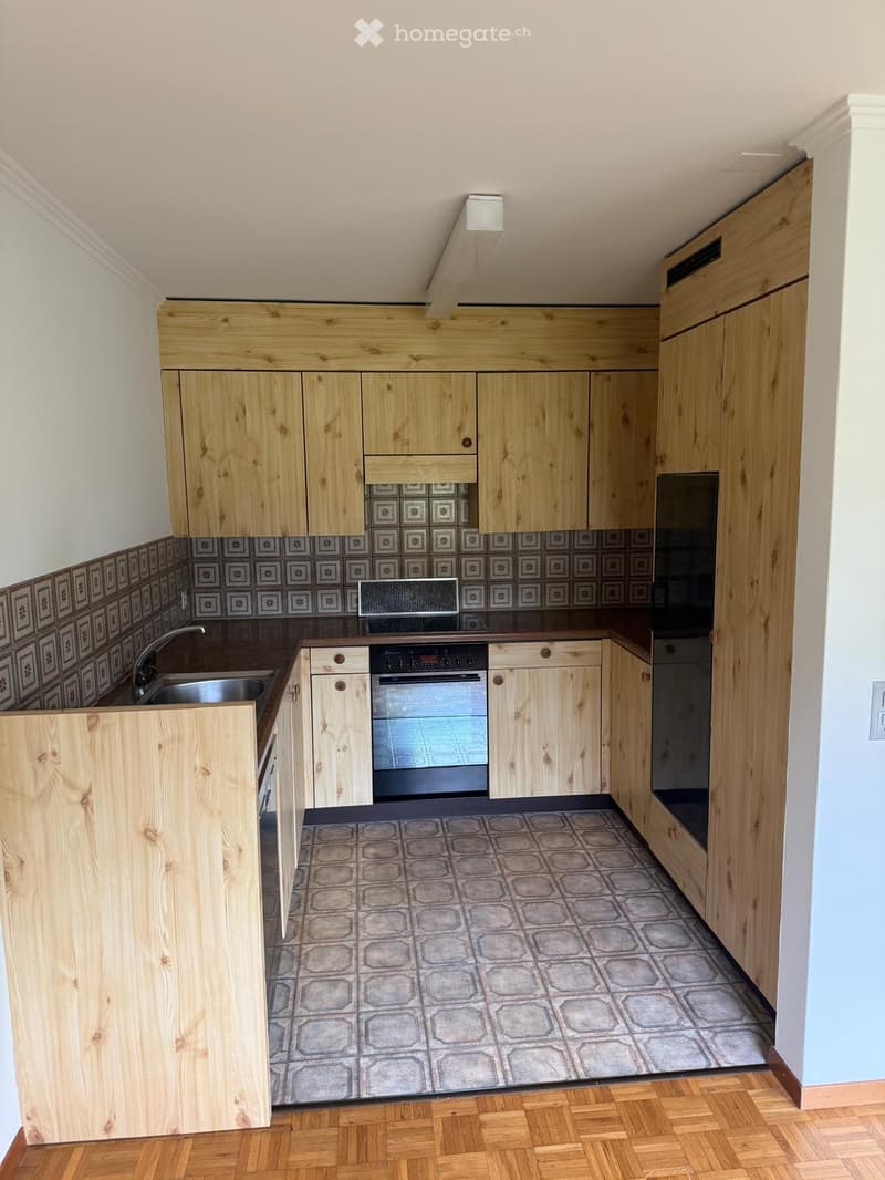 Modern kitchen with wooden cabinets, stainless steel sink, oven, microwave, and tiled backsplash.