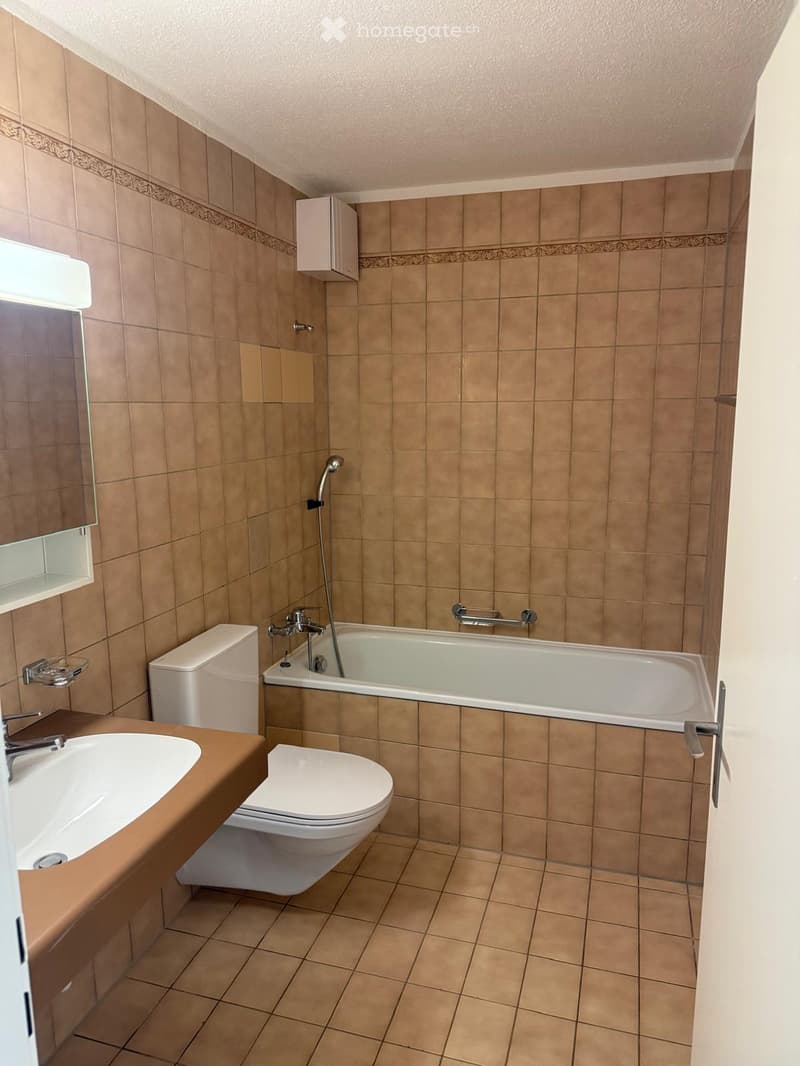 Bathroom with beige tiled walls and floor, featuring a sink, toilet, bathtub, and mirror with a medicine cabinet above it.