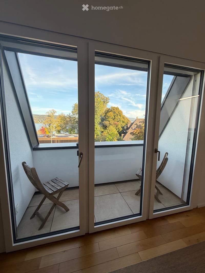 Balcony with wooden chair, sliding glass doors, tiled floor, and scenic view of trees and buildings.