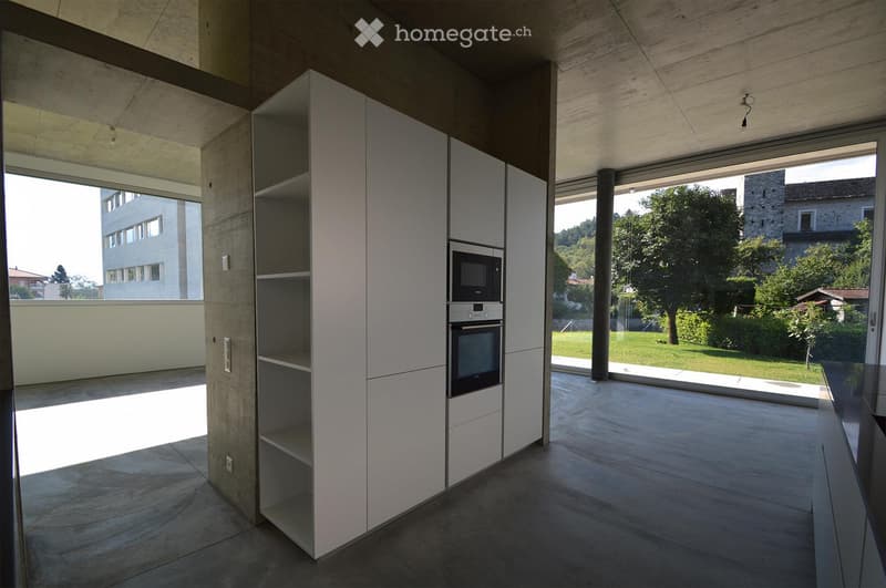 Modern kitchen with white cabinets, microwave, oven, and large windows overlooking a green area.