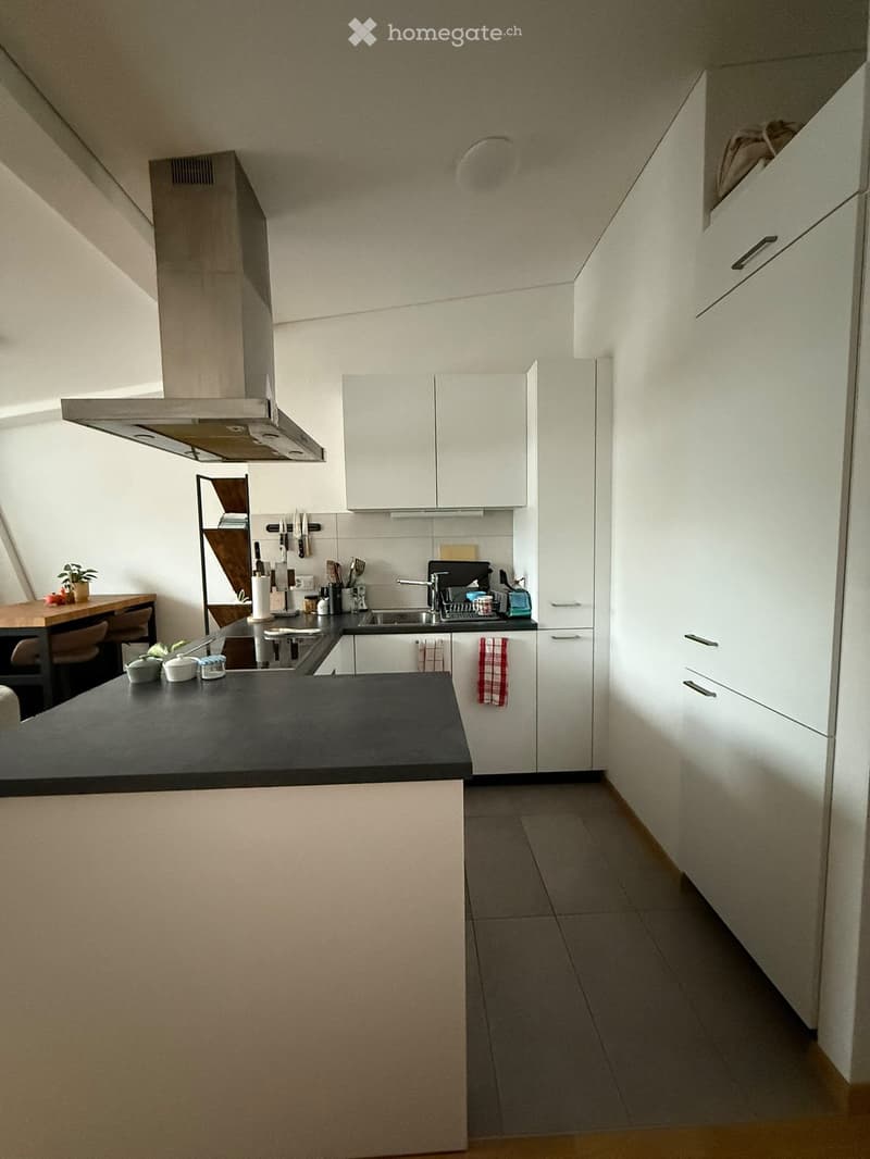 Modern kitchen with white cabinets, stainless steel appliances, black countertop, and a small dining area with a table and chairs.